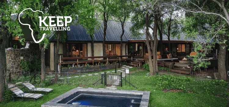 Nature-focused travel lodge with shaded trees, a pool in the foreground, and warm outdoor seating areas